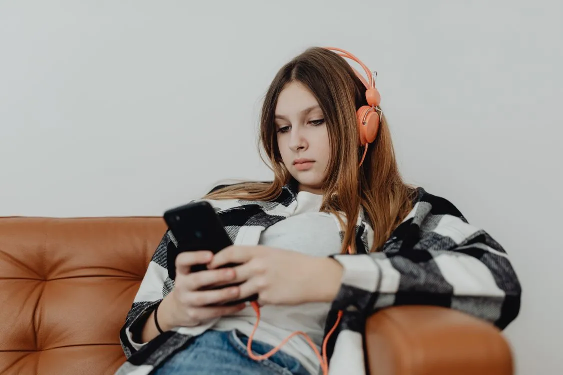 Teenage girl wearing headphones and looking at a smartphone on a sofa